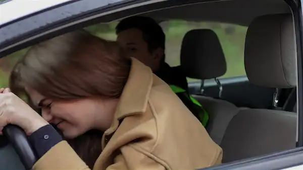A young woman sitting crying and frustrated after her infertility appointment. Her head rests on the steering wheel of her care.